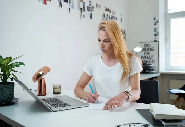 Freelancer mulher escreve documento com um lápis sentado à mesa — Fotografia de Stock