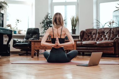 Oturma odasında yerde yoga yapan sporcu kadının arka görüntüsü.
