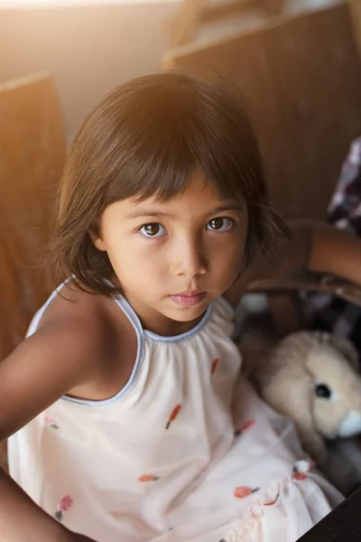 Маленькая девочка смотрит на камеру в платье сидя на стуле в комнате — стоковое фото