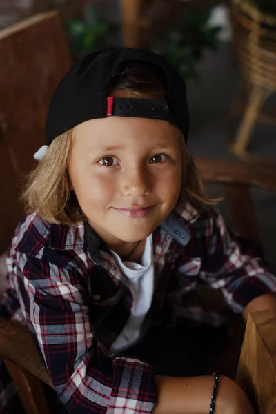 Sonriente chico con gorra se sienta en la silla mirando a la cámara en la habitación — Foto de Stock