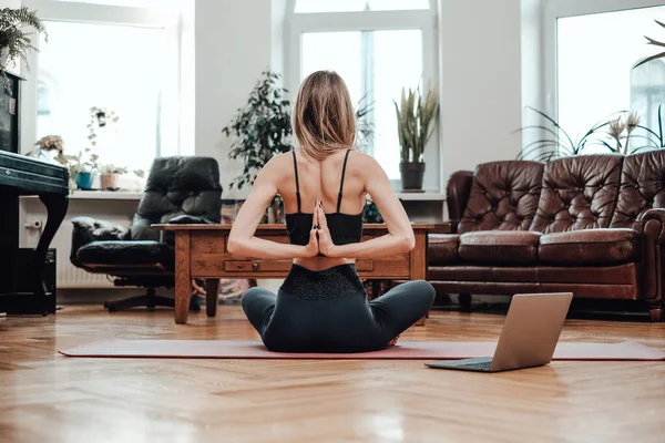 Oturma odasında yerde yoga yapan sporcu kadının arka görüntüsü.