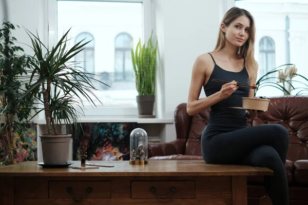 Chica de fitness sosteniendo palos y ensalada posa en la mesa en la sala de estar — Foto de Stock