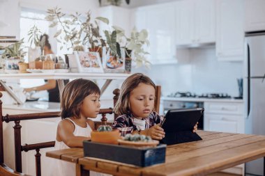 Küçük çocuk ve kız kardeşi oturma odasında dijital tablet kullanıyorlar.