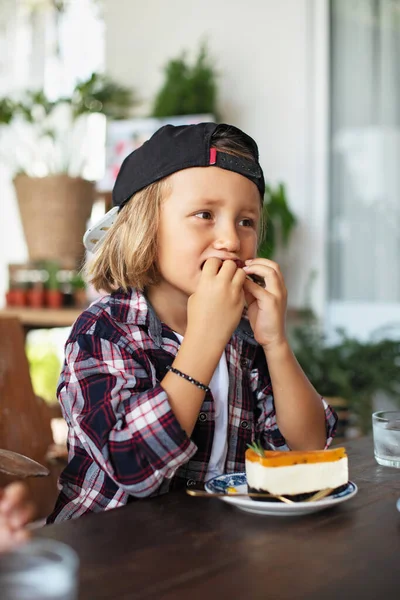 Ragazzo allegro mangia torta gustosa seduto a tavola in appartamento — Foto Stock