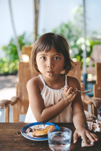 面白い女の子は見てカメラ食べるデザートでテーブルでカフェ — ストック写真