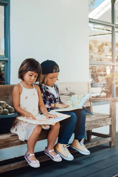 Serious boy and girl read a book sitting on park bench in daytime — Stock Photo, Image