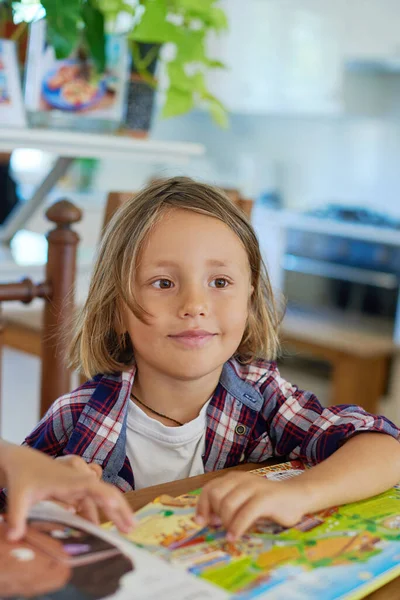 Gioioso ragazzo con libri si siede a tavola e distoglie lo sguardo nella stanza — Foto Stock