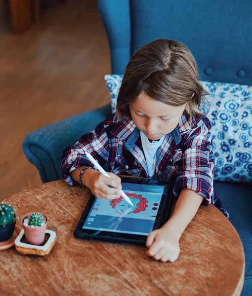 Liten unge med modern utrustning målar konst vid bordet på fåtölj — Stockfoto