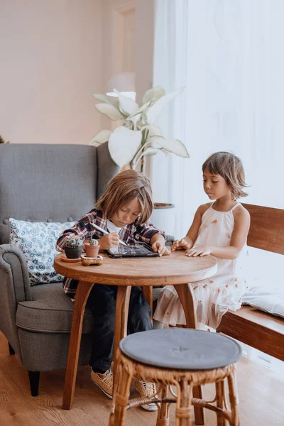 Menino e menina com lápis digital e tablet à mesa na sala de estar — Fotografia de Stock