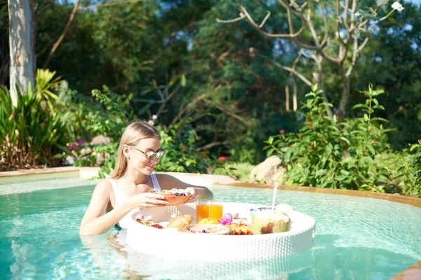 Femme gaie avec des lunettes de soleil se détend dans la piscine et mange de la nourriture — Photo