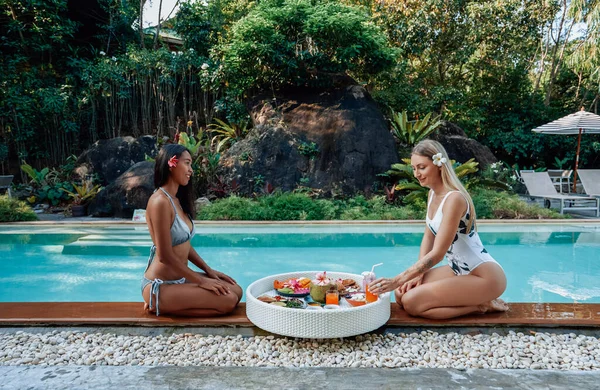 Deux femmes gaies mangent et boivent de la nourriture asiatique autour de la piscine — Photo