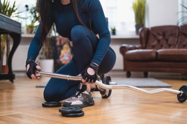 Spor kıyafetleri giymiş bir kadın salonda halter hazırlıyor.