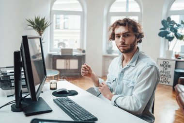 Kıvırcık saçlı ve sakallı neşeli adam masada oturup bilgisayar çalışıyor.