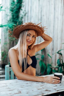 Hasır şapkalı mutlu kadın tatillerinde masada oturuyor.