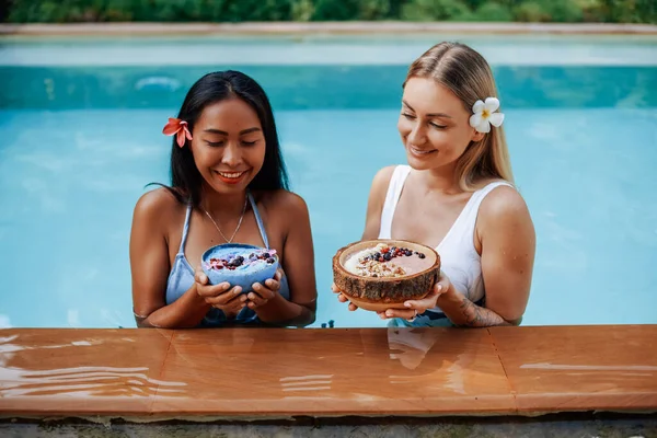 Glada kvinnor med hålla tallrikar med bär mat pose på kameran i poolen — Stockfoto