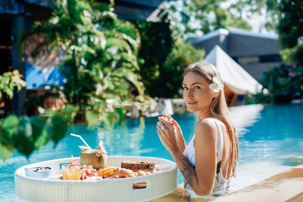 Femme séduisante pose dans la piscine en regardant la caméra avec table flottante — Photo