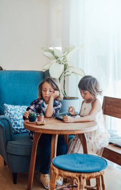 Oturma odasında tabletli ve kalemli iki çocuk.