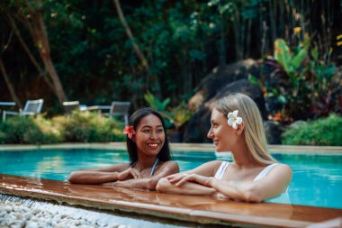Cheerful girls in bikini swim in pool and enjoy journay in Thailand clipart