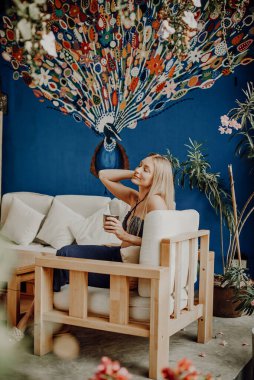 Bardaklı rahat bayan gezgin mavi duvarlı sandalyede oturuyor.