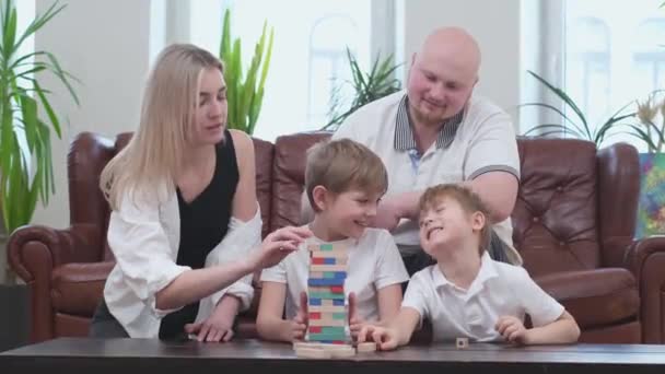 Família feliz de quatro pessoas jogando no jogo de tabuleiro, torre de madeira — Vídeo de Stock