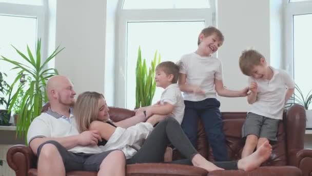 Tři bratři se lechtají, šťastní rodiče se dívají, jak sedí na gauči — Stock video
