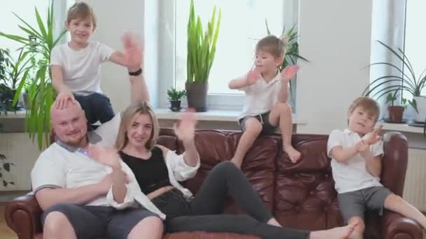 Tre leende pojkar och glada föräldrar vinkar åt kameran sittandes på soffan — Stockvideo