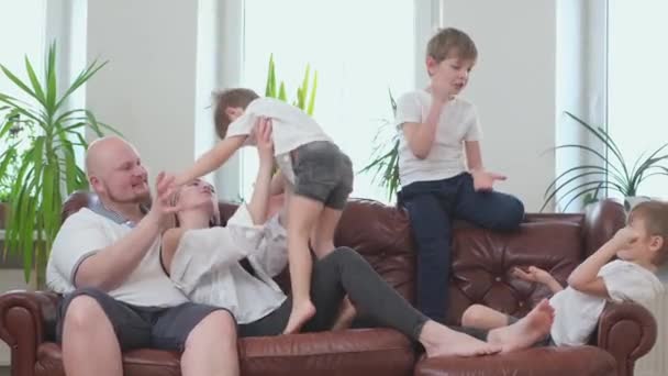 Három aktív testvér és boldog szülő játszik a kanapén. — Stock videók