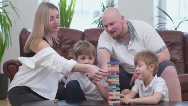 Happy parents and two joyful sons playing in board game, wooden tower — Stock video