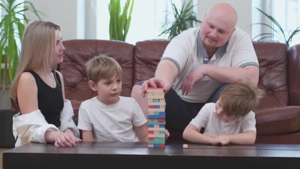 Família feliz de quatro pessoas jogando no jogo de tabuleiro, torre de madeira — Vídeo de Stock