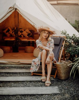 Hasır şapkalı olumlu genç kadın çadırın arkasında poz veriyor.