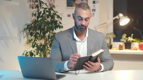 Seriöser Geschäftsmann macht sich Notizen im Notizbuch, während er zu Hause arbeitet — Stockvideo