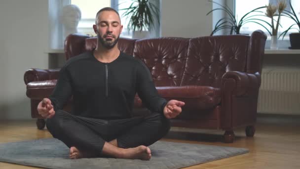 Férfi gyakorló jóga póz a stúdióban növények mellett a bőr kanapé — Stock videók