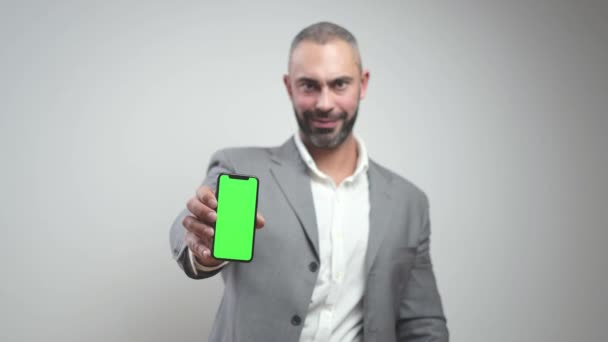 Leende affärsman håller mobil med grön skärm och visar för kameran — Stockvideo