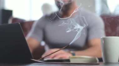 İş adamı çalışıyor, daktilo yazıyor, tütsü içiyor.