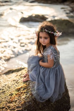 Sevimli anaokulu kızı Tayland 'da deniz kıyısında bir kayanın üzerinde oturuyor.