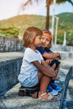 Neşeli çocuk kameraya bakar ve kız kardeşiyle kaykay yaparken gülümser.