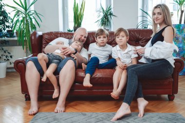 Modern apartmandaki koltukta oturan neşeli aile ve kamera önünde poz vermek.