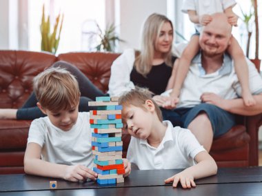 İki neşeli çocuk anne babalarının arka planında Jenga oynuyorlar.