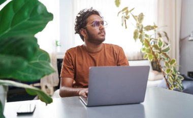 Serious and bearded guy uses a laptop sitting at table in cosy room