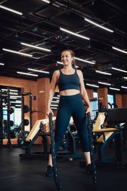 Siyah giysili neşeli kadın spor salonunda ipleri tutuyor.