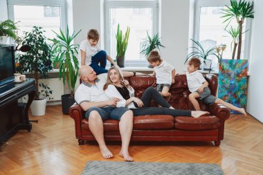 Modern apartmandaki koltukta oturan neşeli aile ve kamera önünde poz vermek.