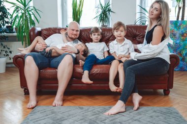 Modern apartmandaki koltukta oturan neşeli aile ve kamera önünde poz vermek.