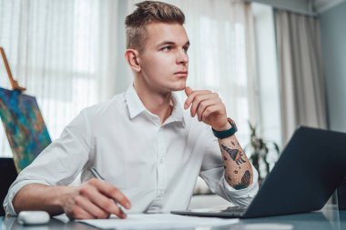 Ofis çalışanı masa başında kağıt ve dizüstü bilgisayarla oturuyor.