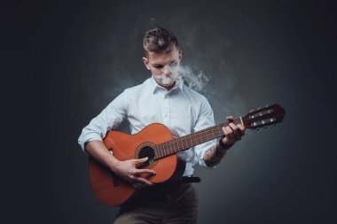 Arka planda sigara içen dövmeli genç bir gitarist.