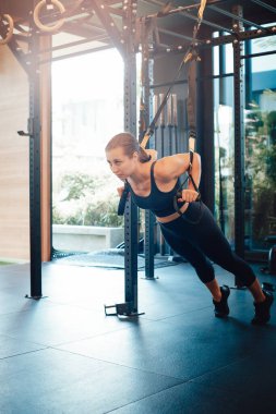 Dişi sporcu antrenman aparatlarıyla fiziksel egzersiz yapıyor.