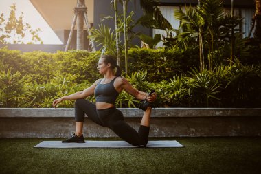 Dişi sporcu dışarıda huzurlu bir yerde ısınıyor.