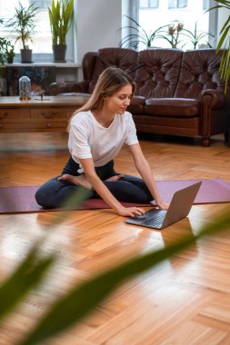 Yoga yapan kadın laptopunu paspasın üzerinde kullanıyor.
