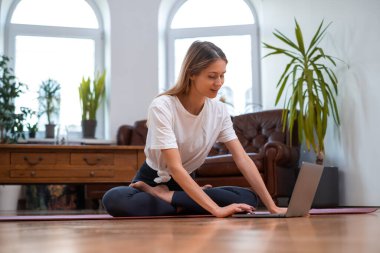 Yoga yapan kadın laptopunu paspasın üzerinde kullanıyor.