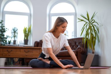 Yoga yapan kadın laptopunu paspasın üzerinde kullanıyor.