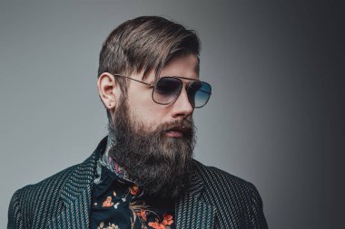 Stüdyoda güneş gözlüklü, şık ve sakallı bir adam.